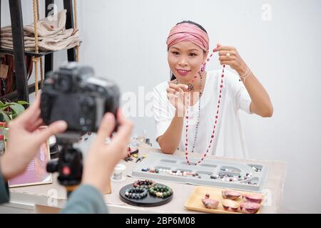 Jeune femme souriante de course mixte montrant un collier en pierre naturelle fait à la main, elle a fait dans l'atelier Banque D'Images