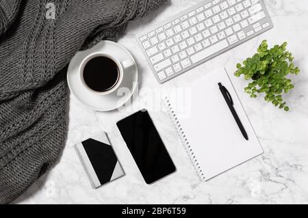 Espace de travail confortable pour la maison. Bureau en marbre avec tissu écossais en laine chaude, tasse de café, clavier, téléphone portable, plante maison verte, papier vierge, carnet et stylo Banque D'Images