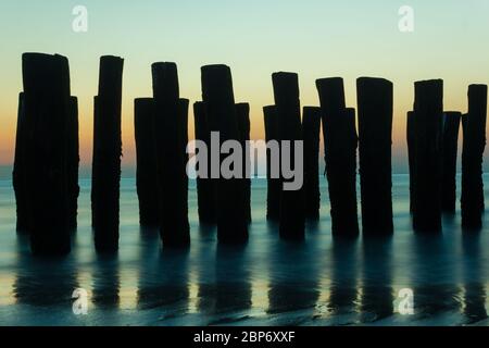 Belle silhouette de poteaux en bois (brise-lames) avec marée montante dans la mer du Nord sur la côte hollandaise Banque D'Images