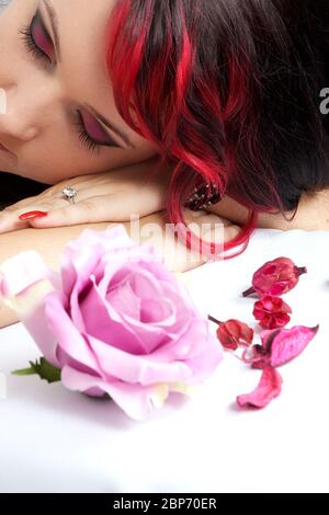 Femme visage avec de longs cheveux noirs et rouges couchés sur ses mains avec des fleurs Banque D'Images