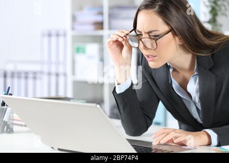 Femme exécutive avec lunettes ayant des problèmes de vue essayant de lire sur un ordinateur portable assis sur son bureau Banque D'Images