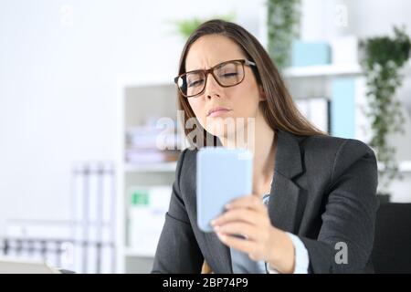 Femme exécutive portant des lunettes avec problème de vue essayant de lire sur un smartphone assis sur son bureau Banque D'Images