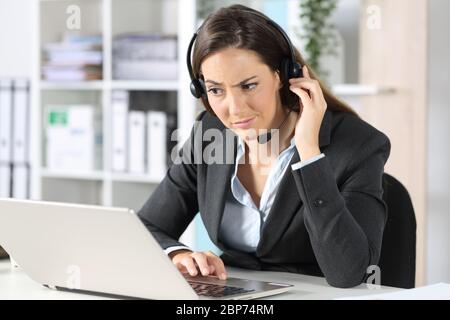 Femme suspecte d'un télévendeur avec un micro-casque regardant un ordinateur portable assis sur un bureau dans le bureau Banque D'Images