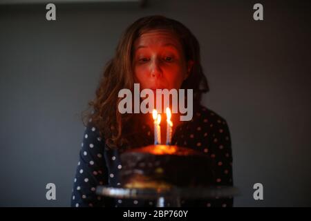 Une femme célèbre son anniversaire en soufflant les bougies sur son gâteau d'anniversaire à Belfast, en Irlande du Nord. Banque D'Images