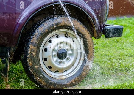 Lavage de voiture dans l'après-midi à l'extérieur avec un jet d'eau d'un tuyau de jardin. Un puissant jet d'eau évacue la saleté du corps violet de la voiture Banque D'Images