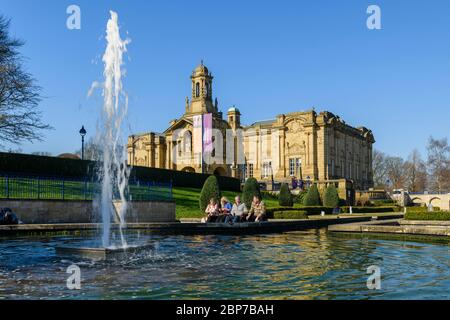 Extérieur de la galerie d'art Cartwright Hall (grand bâtiment historique) et 4 personnes assises près de la fontaine du jardin aquatique Mughal - Lister Park, Bradford, Angleterre, Royaume-Uni Banque D'Images