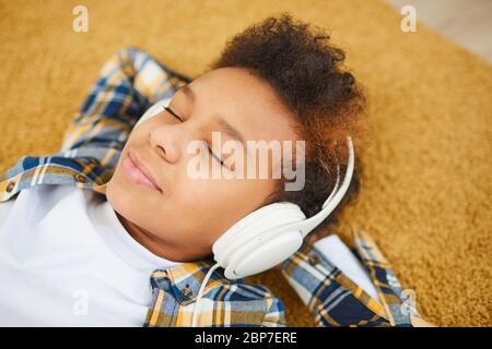 Portrait d'un adolescent africain portant un casque et allongé sur le sol tout en écoutant de la musique avec les yeux fermés, espace de copie Banque D'Images