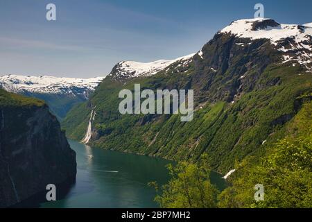 Geirangerfjord, Norvège, a regardé le long du fjord vers les chutes d'eau de Seven Sisters au loin avec des montagnes enneigées autour Banque D'Images