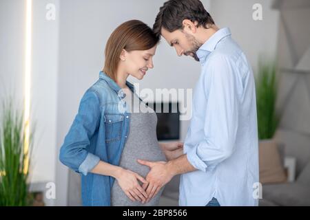 Jeune homme aux cheveux foncés touchant son ventre de femme enceinte Banque D'Images