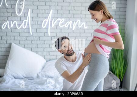 Homme barbu touchant son abdomen enceinte et souriant Banque D'Images
