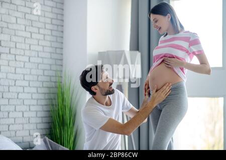 Homme barbu touchant son abdomen enceinte et regardant excité Banque D'Images