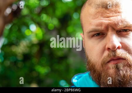 Un homme à barbe chauve regarde la caméra avec une expression curieuse confuse tandis que la lumière du soleil dure frappe la moitié de son visage Banque D'Images