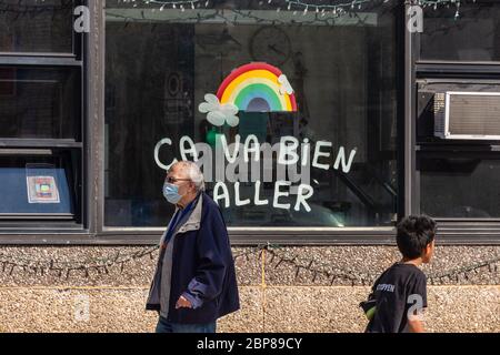 Montréal, CA - 17 mai 2020 : homme mature avec masque facial pour la protection contre la marche COVID-19 devant l'arc-en-ciel dessinant sur la rue Masson. Banque D'Images