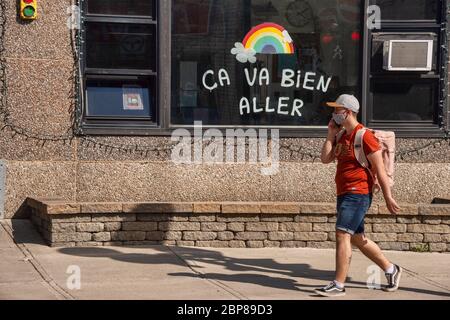 Montréal, CA - 17 mai 2020: Jeune homme avec masque pour la protection contre COVID-19 à vélo devant un arc-en-ciel dessinant sur la rue Masson. Banque D'Images