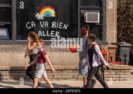 Montréal, CA - 17 mai 2020 : famille avec masques pour la protection contre la marche COVID-19 devant l'arc-en-ciel dessinant sur la rue Masson. Banque D'Images