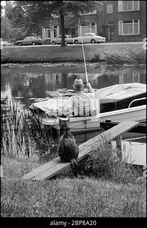 Image historique en noir et blanc d'un pêcheur et d'un chat en attente en 1977, Leiden, pays-Bas Banque D'Images