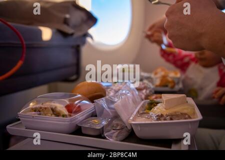 un avion passager en gros plan mange un délicieux repas chaud à bord sur une table pliante. en arrière-plan, il y a une fenêtre dans le hublot. Banque D'Images