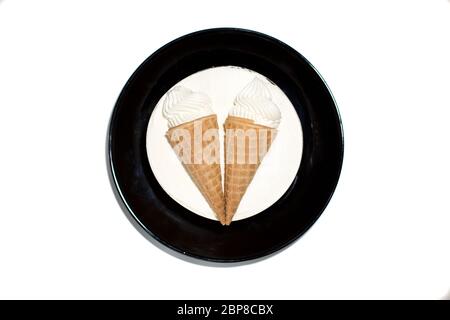 dessert blanc rond isolé gâteau doux et délicieux à la glace avec décoration deux cornets de glace dans une tasse à gaufres sur une assiette noire. vue de dessus, gros plan Banque D'Images