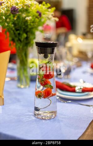 une carafe remplie d'eau et de fraises se trouve sur une table bleue servie. gros plan, mise au point douce. la table servie est sur fond flou Banque D'Images