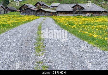 Urnerboden, UR / Suisse - 17 mai 2020: Route de montagne en gravier menant à de vieilles granges et chalets alp dans le village d'Urnerboden dans les Alpes suisses en c Banque D'Images