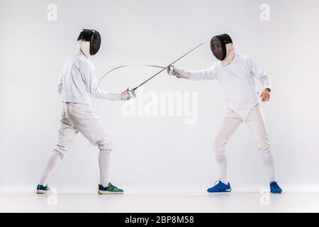 Les deux hommes en tenue d'escrime pratiquant avec épée contre fond studio gris Banque D'Images