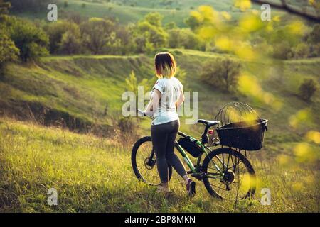 Jeune femme s'amusant près du parc de campagne, à vélo, voyageant le jour du printemps. Nature calme, jour de printemps, émotions positives. Activité sportive et de loisirs. Marche en mouvement, nature en pleine floraison. Banque D'Images