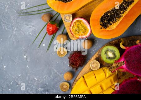 Un ensemble de papaye, de fruits de dragon, de rambutan, de tamarin, de mangue, de fruits de passion, de kiwi, d'orange, de fraise, de feuilles vertes sur fond de pierre grise avec spa copie Banque D'Images