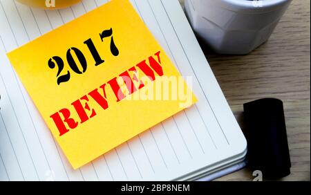 L'écriture de texte montrant l'examen 2017. Concept d'affaires de rapport de synthèse annuel written post-it papier, fond en bois avec copie espace, café et Banque D'Images