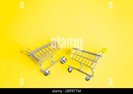 Deux petits chariots de supermarché en métal miniature pour faire du shopping isolés sur fond jaune de couleur menthe. Vue de dessus. Espace de copie pour le texte. Achats, Banque D'Images