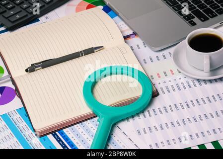 Bureau d'un homme d'affaires. Une loupe sur un Bloc-notes, un ordinateur, une tasse de café et des tables avec des finances. Documents et statistiques de l'entreprise Banque D'Images