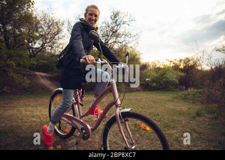 Jeune femme s'amusant près du parc de campagne, à vélo, voyageant le jour du printemps. Nature calme, jour de printemps, émotions positives. Activité sportive et de loisirs. Marche en mouvement, nature en pleine floraison. Banque D'Images