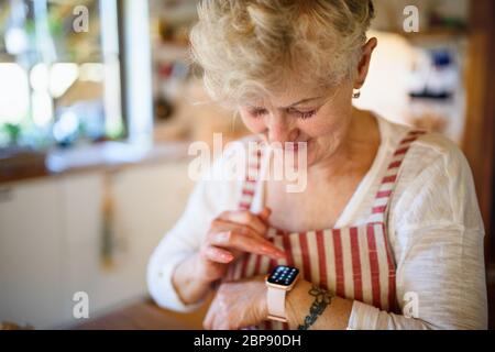 Femme âgée avec tablier à l'intérieur à la maison, utilisant la montre intelligente. Banque D'Images