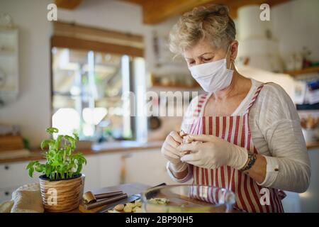 Femme avec masque et gants de cuisine à l'intérieur à la maison, concept de virus corona. Banque D'Images