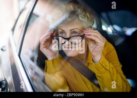 Femme âgée avec des lunettes dans une voiture. Filé à travers le verre. Banque D'Images