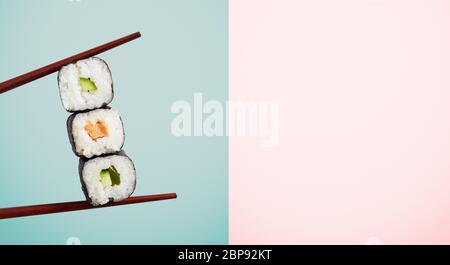 Baguettes contenant trois enveloppements d'algues avec du riz et de l'avocat sur fond bleu moitié de deux tons. Inclut l'espace de copie. Banque D'Images