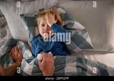 Le père s'est fait soigner sur un petit fils malade allongé dans un lit à l'intérieur à la maison. Banque D'Images