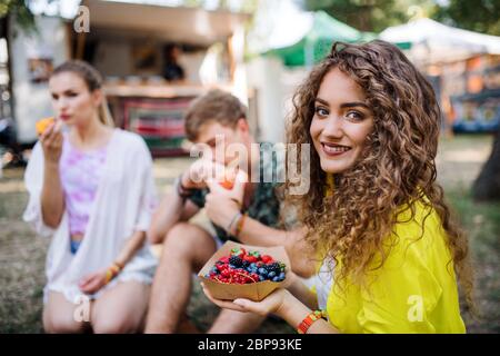 Belle jeune fille assise sur terre au festival d'été, manger. Banque D'Images