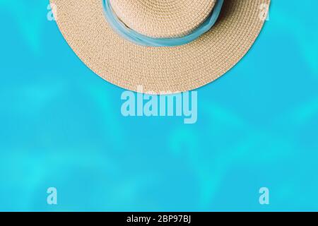 Vue de dessus d'un chapeau de plage en paille avec foulard bleu sur fond d'eau. Concept été minimal avec espace de copie. Banque D'Images