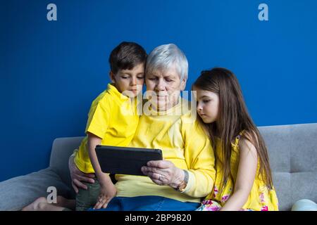 Une vieille grand-mère et ses petits-enfants bien-aimés s'assoient à la maison et prennent des photos sur leur smartphone Banque D'Images