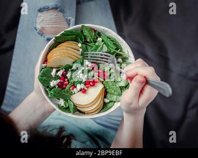 Femme en jeans holding vegan saladier avec les épinards, poire, pomme grenade, fromage. Le petit-déjeuner végétarien, végétalien, régime alimentaire concept. Jeune fille en jeans holding Banque D'Images