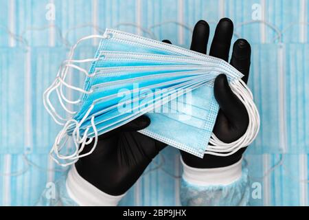 L'homme médical tient lot bleu masques respiratoires chirurgicaux dans un gant de protection noir dans deux mains. Image de concept sur les bandages respiratoires de fond Banque D'Images