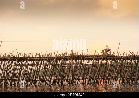 Un cycliste traverse un pont de bambou au-dessus du Mékong au coucher du soleil. Ko Pen, Cambodge, Asie du Sud-est Banque D'Images