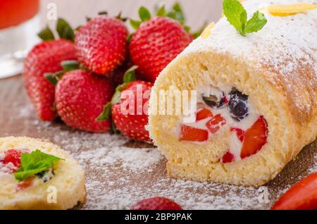 Rouleau d'éponge avec fraises et bleuets, tous les fruits frais, saupoudrer de feuilles de menthe Banque D'Images