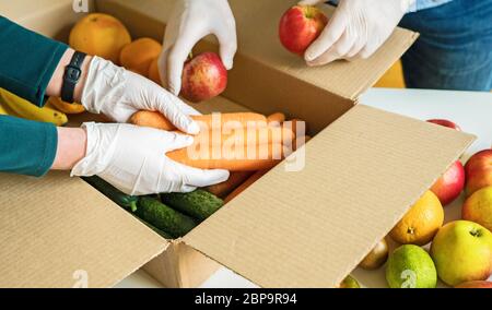 Les bénévoles en gants médicaux de protection mettent les fruits et les légumes dans la boîte de dons. Banque D'Images