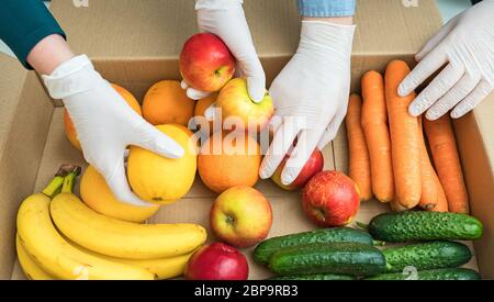 Les bénévoles en gants médicaux de protection mettent les fruits et les légumes dans la boîte de dons. Banque D'Images