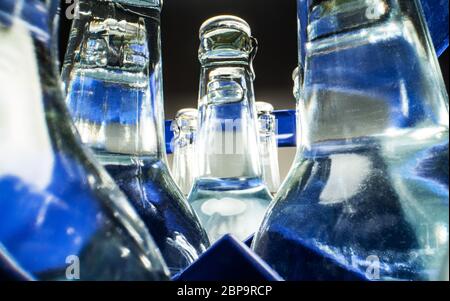 Gros plan du boîtier bleu de bouteilles en verre transparent remplies d'eau minérale. Banque D'Images