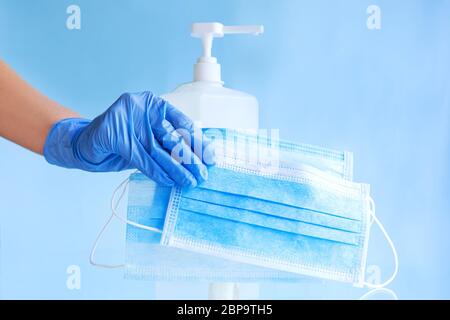 Masques médicaux, masque chirurgical de protection jetable dans la main du médecin dans des gants bleus. Bouteille de gel désinfectant pour alcool. Coronavirus covid 19 virus Banque D'Images