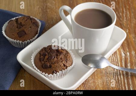 Une vie encore minimaliste dans des tons blancs d'un cupcake au chocolat et d'une tasse de chocolat chaud. Sur fond en bois. Vue horizontale. Banque D'Images