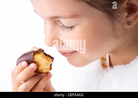 Petite fille goût la pâtisserie d'eclair comme un pro - odeur, morsure, manger. Banque D'Images