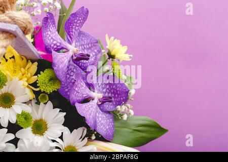 Beau bouquet de fleurs dans un panier en bois lilas sur fond violet. Orchidées, chrysanthèmes, nénuphars, chamomiles composition florale Banque D'Images